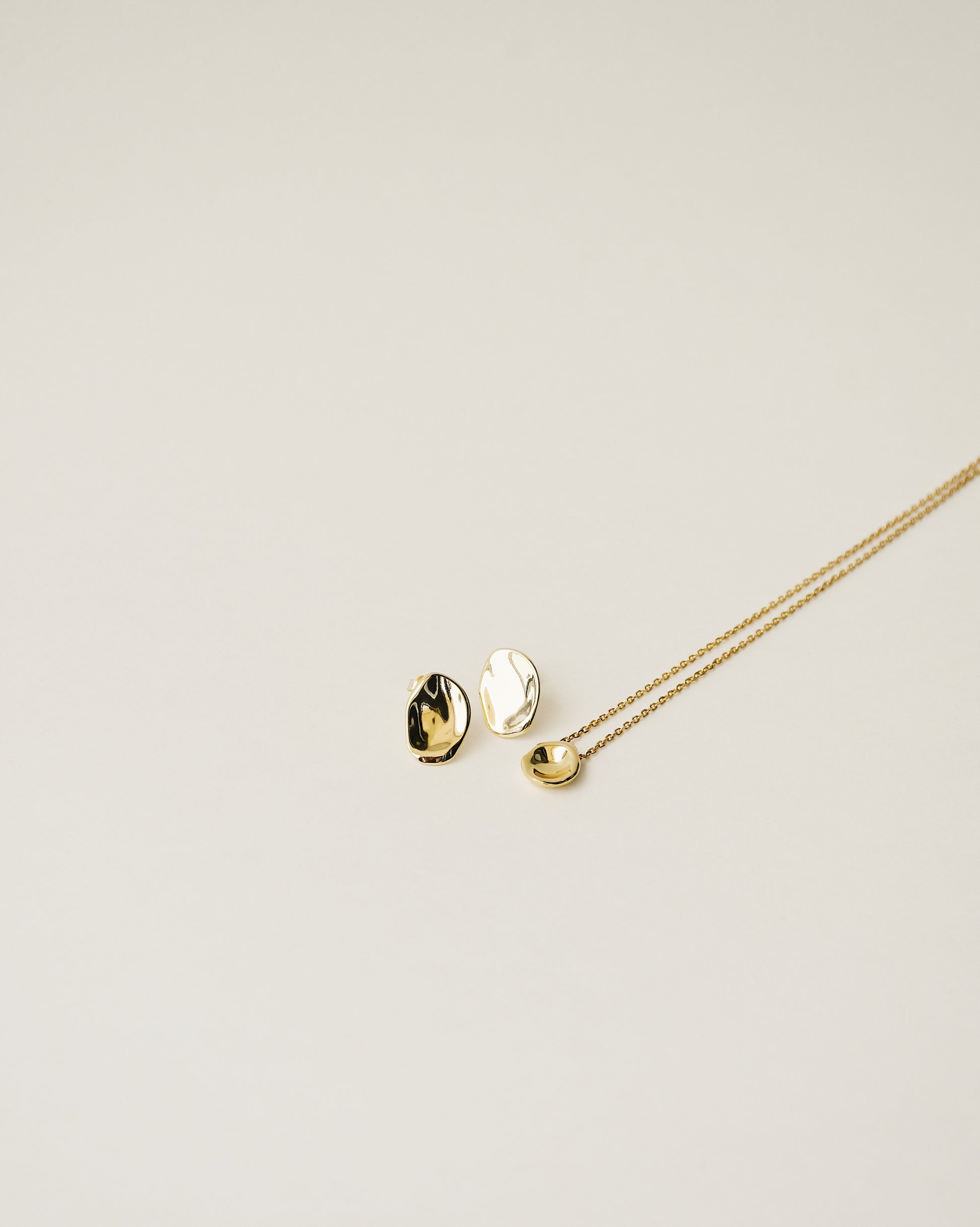 irregularly shaped tiny pendant necklace and stud earrings handcrafted from 925 sterling silver plated in 18k gold. 2020 slow fashion trend.